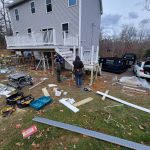 Construction workers installing a deck with a Reeds dumpster on site