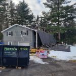 Workers removing the shingles off of a house's roof with a Reeds dumpster on site